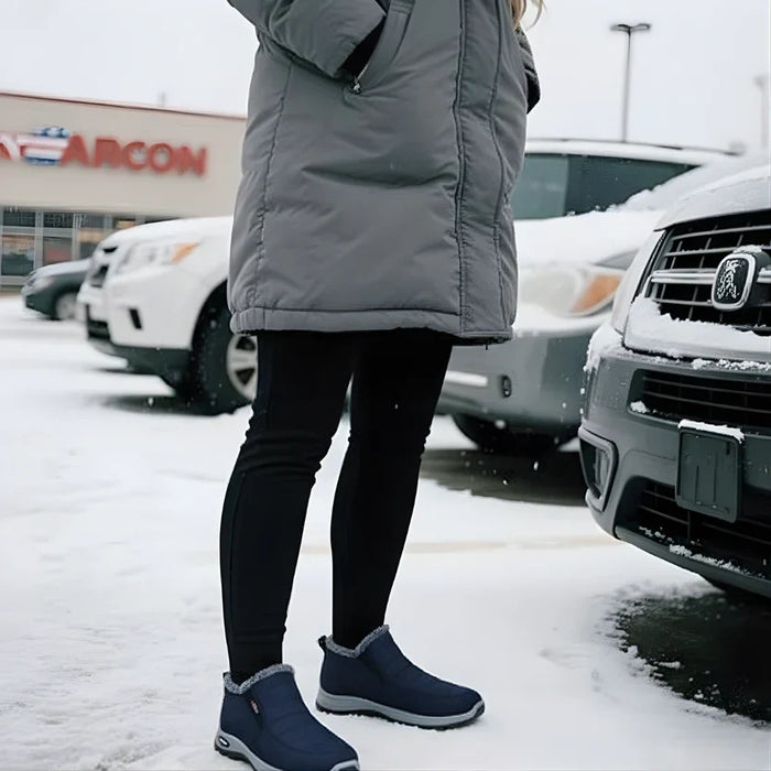 A woman in a winter coat standing in the snow beside her car, wearing blue Sianna boots