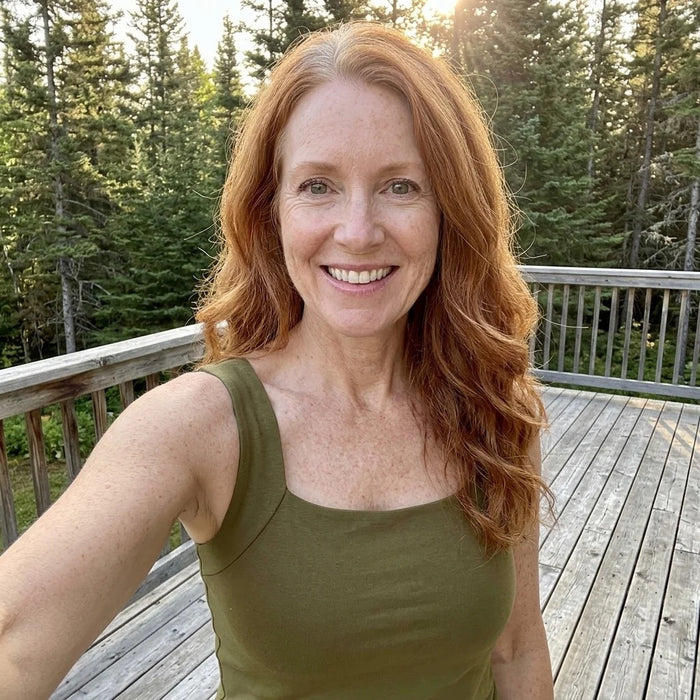 A woman on a wooden deck among pine trees, wearing the Faye Built-In Support Tank in Sage